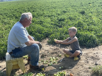 Image of Keesling Farms Growers for Red Gold Tomatoes Kim Keesling wife holding grandchild at the back of a school bus