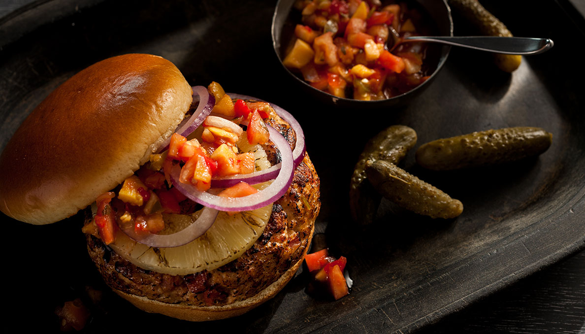 Caribbean Burger Overhead Image of Caribbean Burger with sliced pineaple sliced onions and tomato salsa and pickles