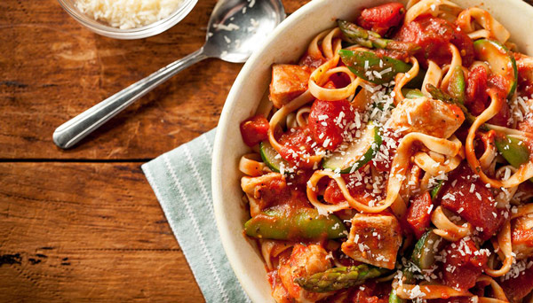 Image of chicken primavera pasta dish with vegetables and tomatoes on platter with parmesan cheese