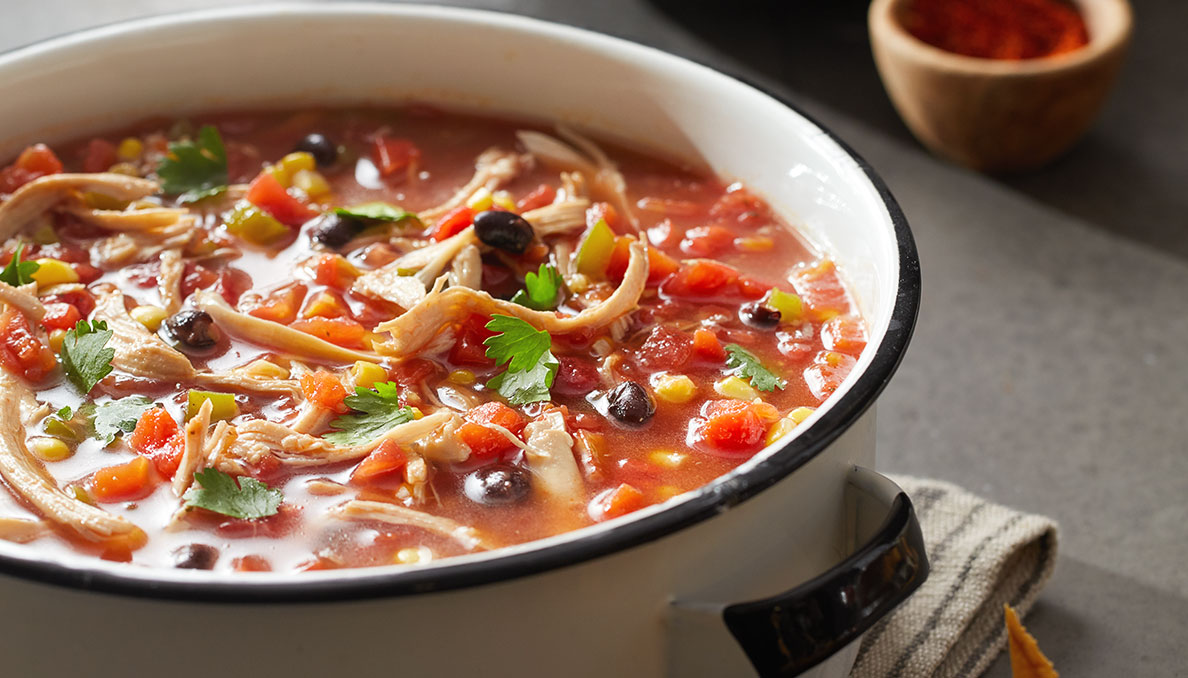 Image of Chicken Tortilla Soup showing diced tomatoes, black beans corn and cilantro with tortilla strips