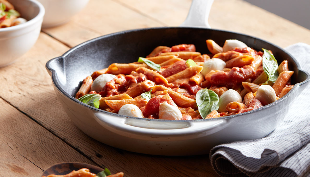 Image of Creamy Caprese Pasta with penne pasta mozzarella balls basil and torn whole peeled tomatoes in skillet