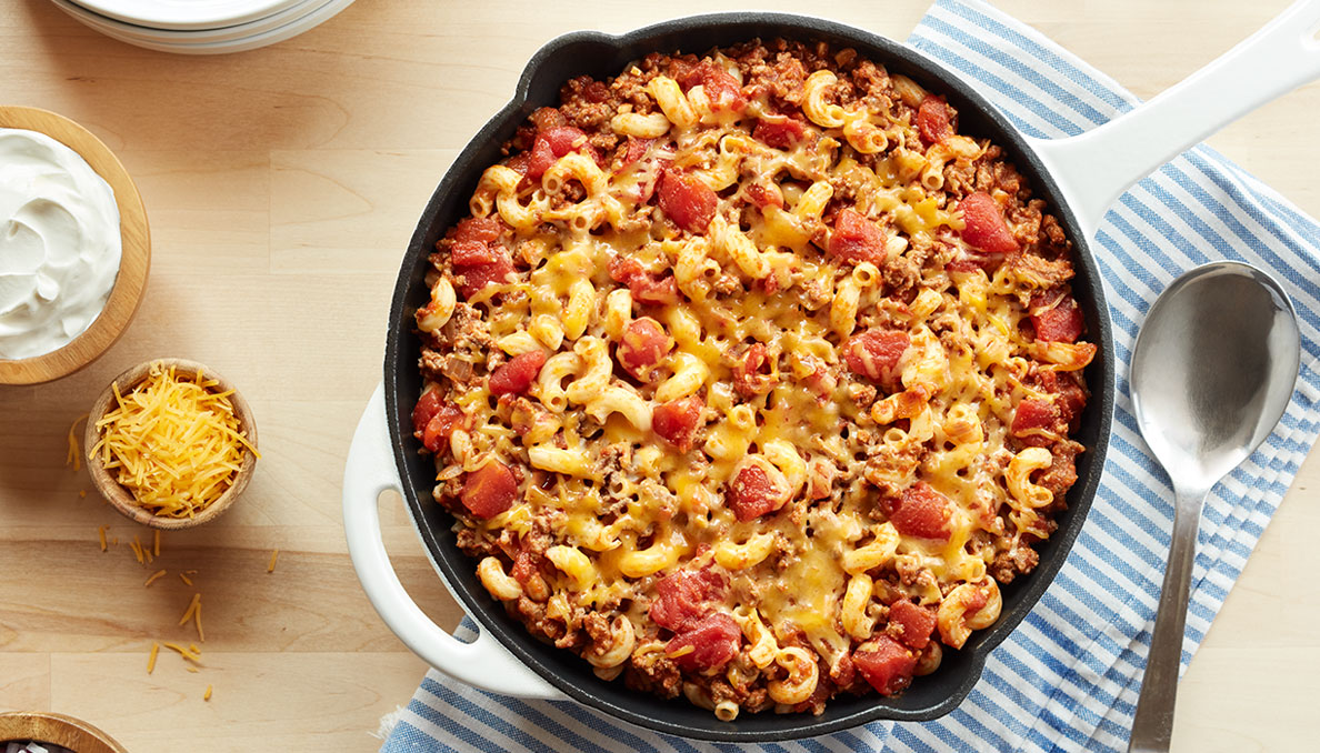 Image of Easy One Skillet Chili Mac in skillet with sour cream and shredded cheese