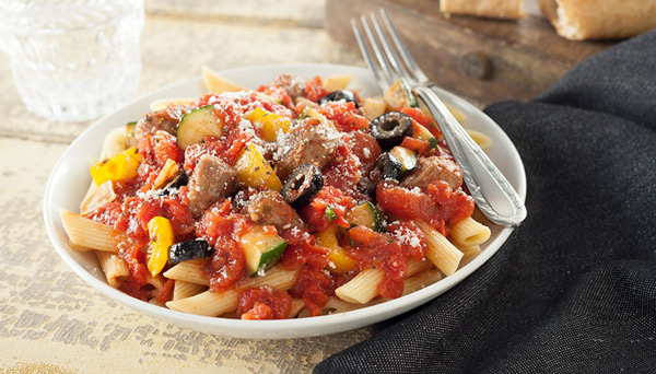 Image of marinara with sausage olives zucchini in a white bowl on a wood table