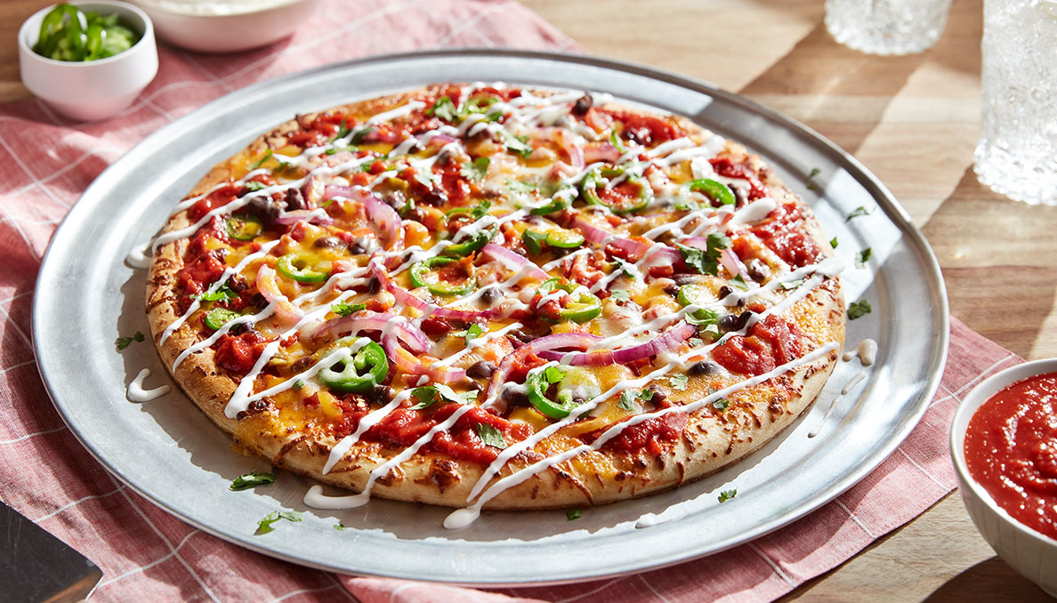 Image of mexican flavored pizza with jalapenos, cheese, black beans, red onion, crushed tomatoes and sour cream drizzle
