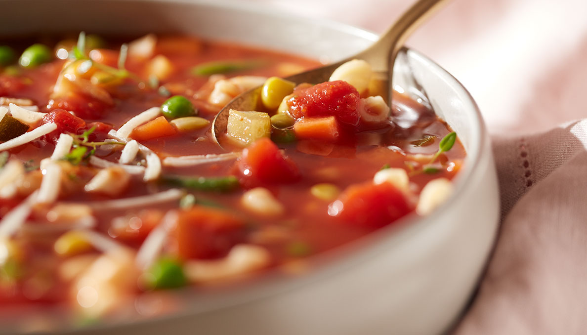 Close up image of minestrone soup in a white bowls with a spoon using canned diced tomatoes