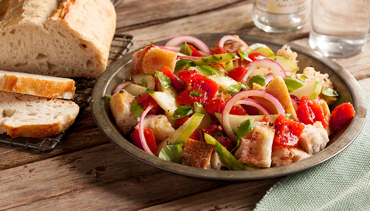 Image of panzanella bread salad in metal pan with sliced bread in the background