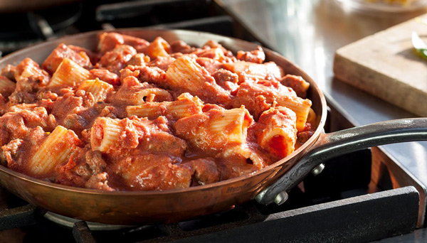 Image of vodka sauce using canned crushed tomatoes in a skillet with rigatoni on stovetop close up view