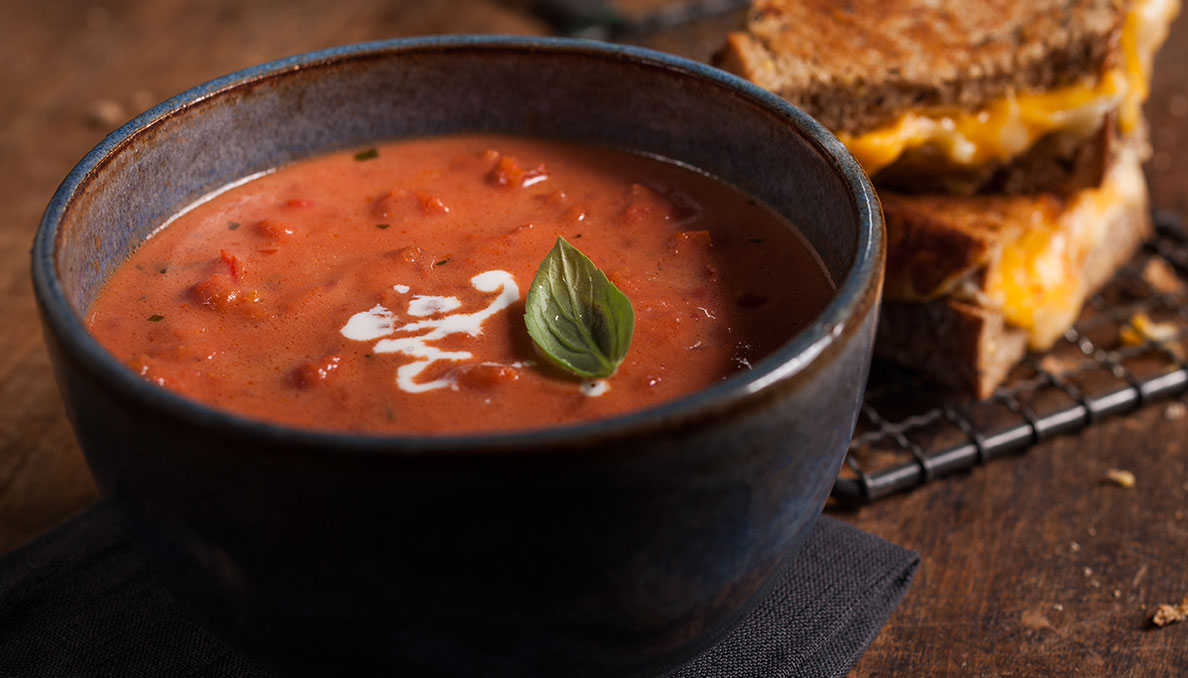 Image of Tomato basil soup with grilled cheese in the background