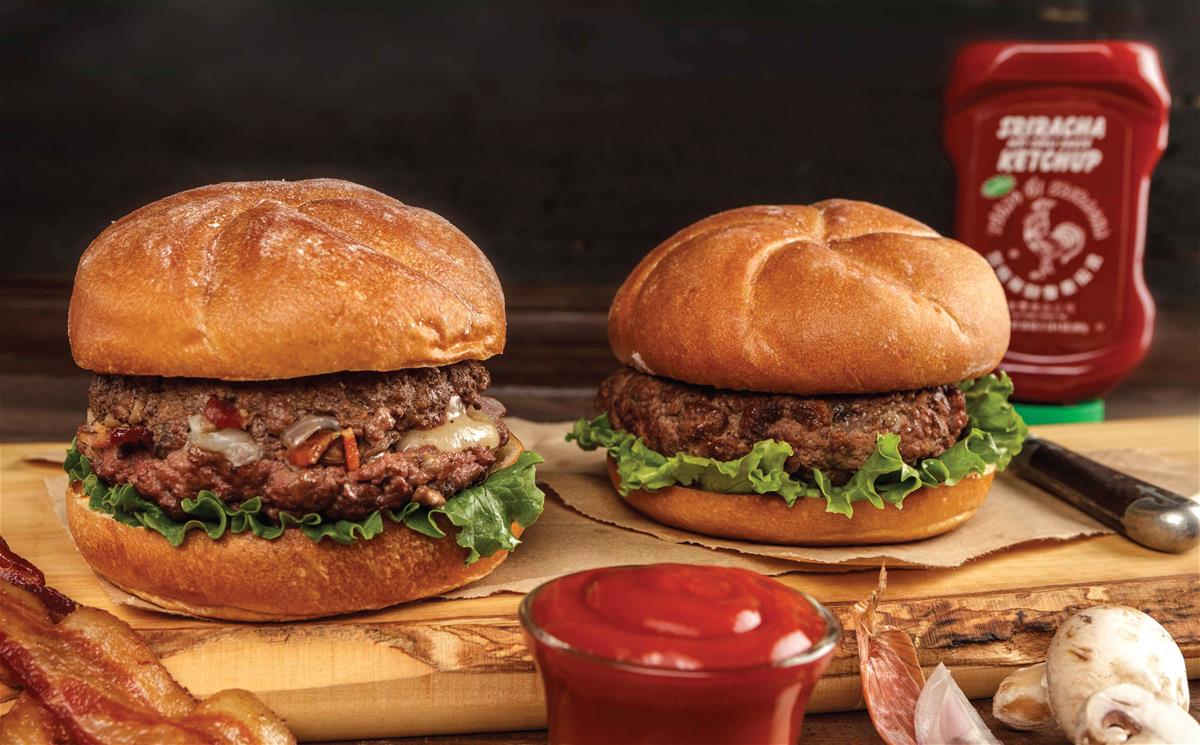 Image of two burgers and red gold sriracha ketchup bottle in background