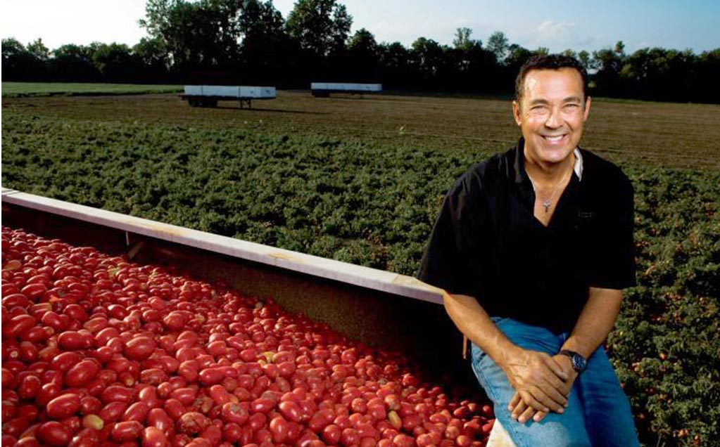 Image of grower sitting on side of tomato trailer full of red tomatoes from tomato field